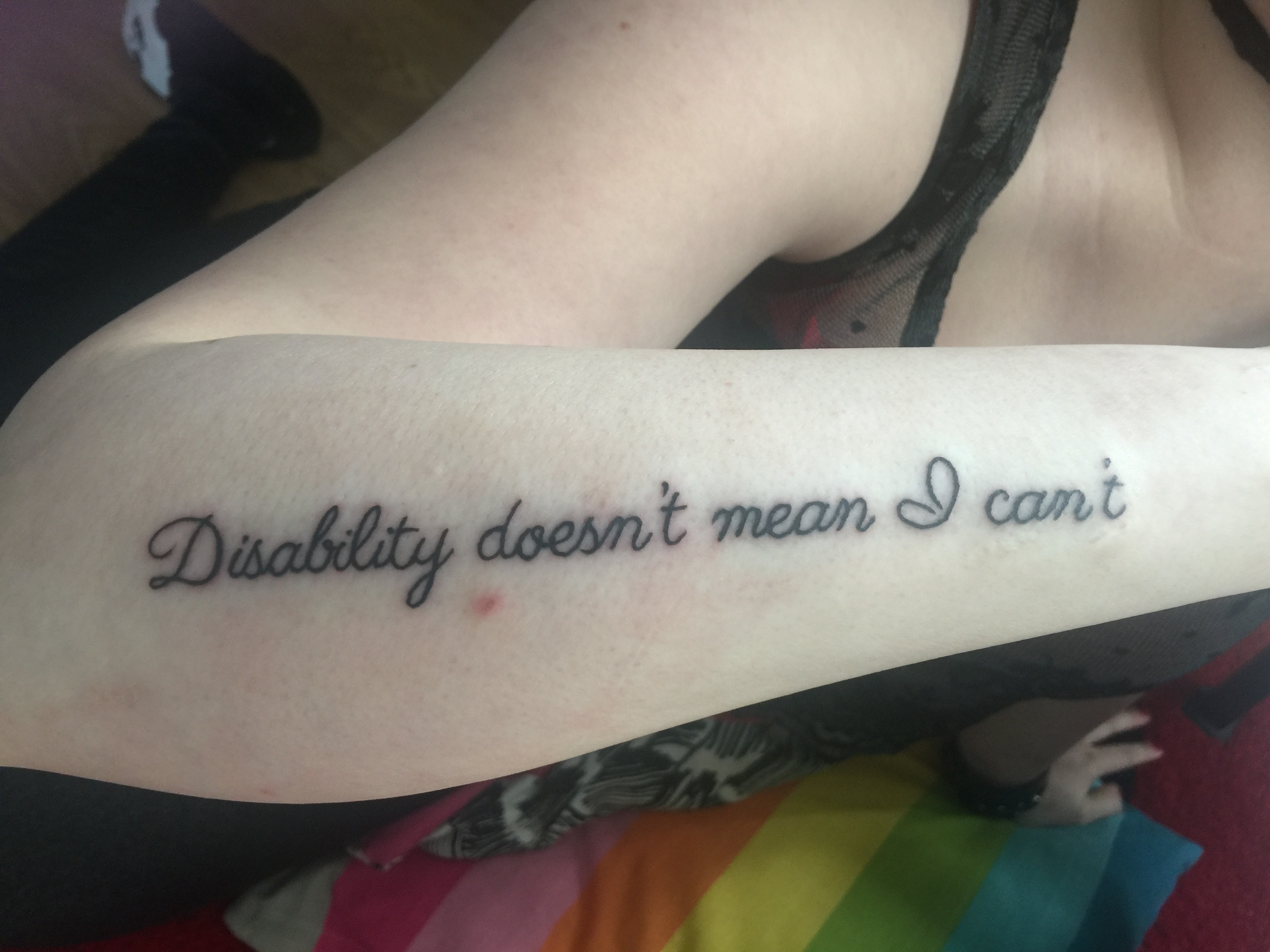 Image description: holding my arm up to camera, showing the tattoo down my forearm reading "disability doesn't mean I can't".