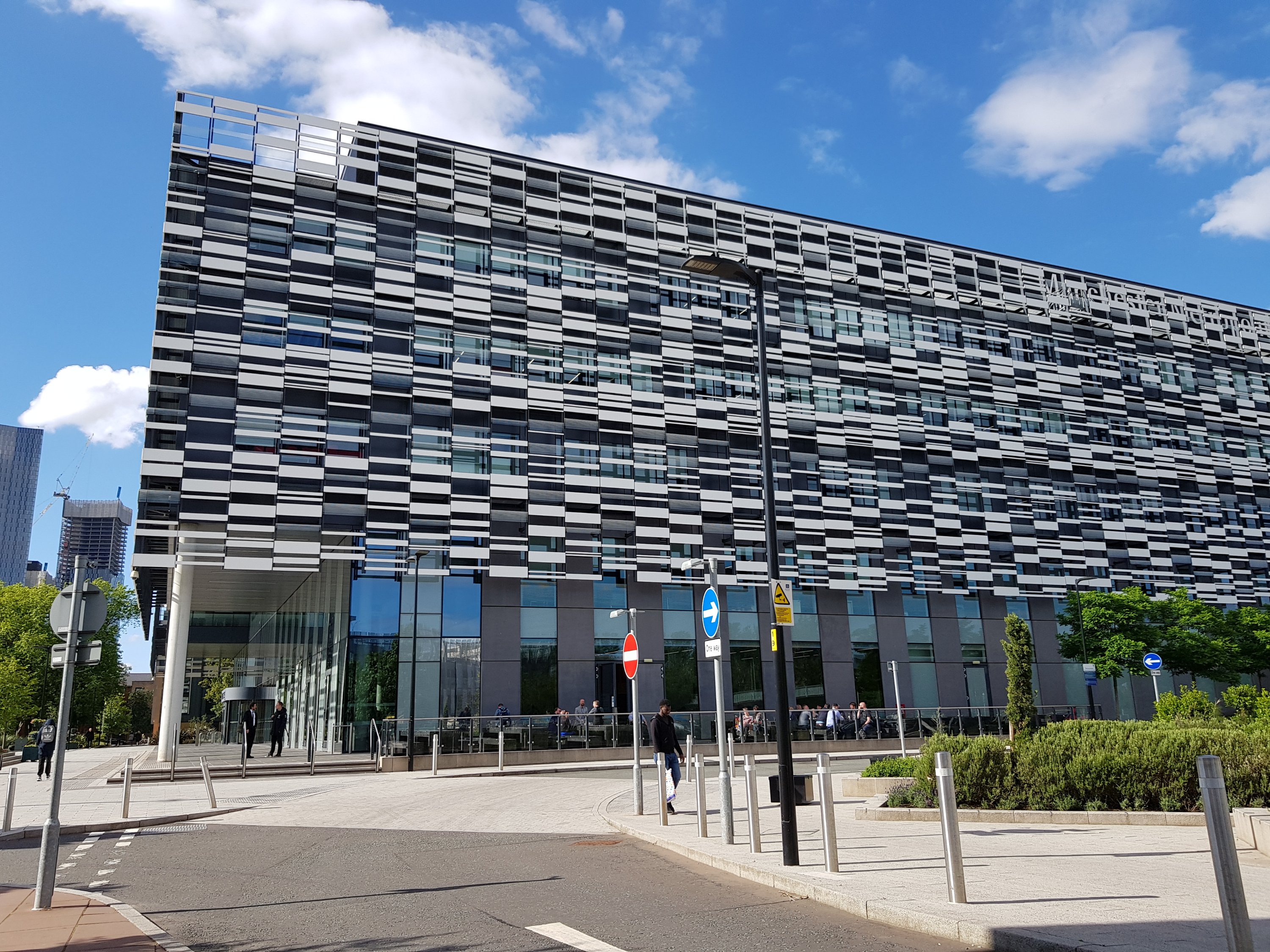 Outside the building. Taken from across the road under a blue sky, this photo shows the block building with a glass front, & grey tiles patterning the other walls.