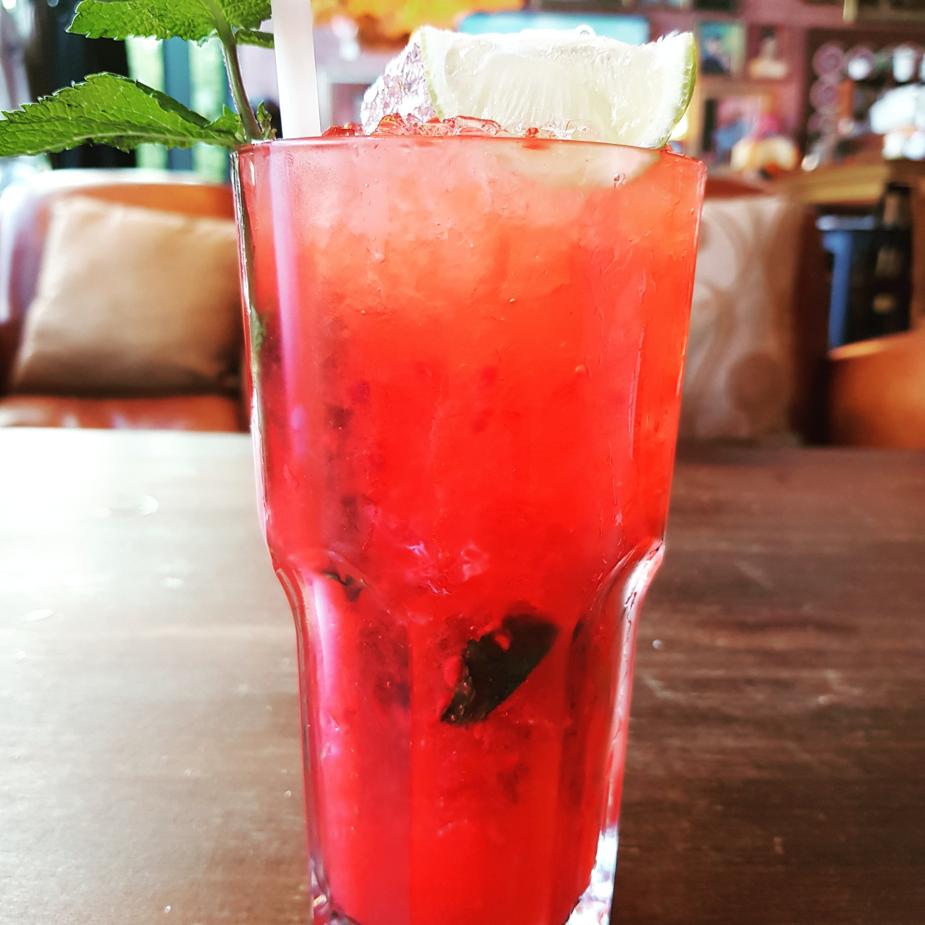 A red berry mojito, mint leaf included, in a tall glass.