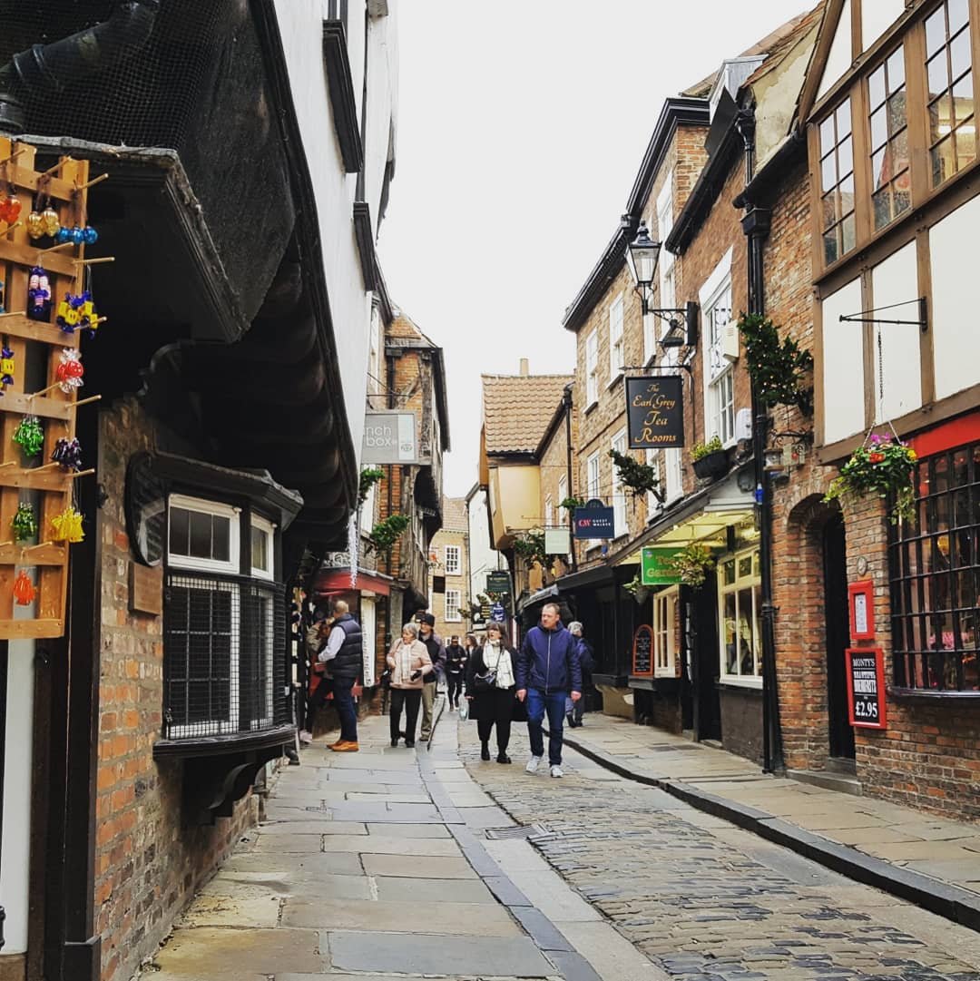 Sat on the cobbled pavement looking down the Shambles. Several people are milling around doing some shopping.