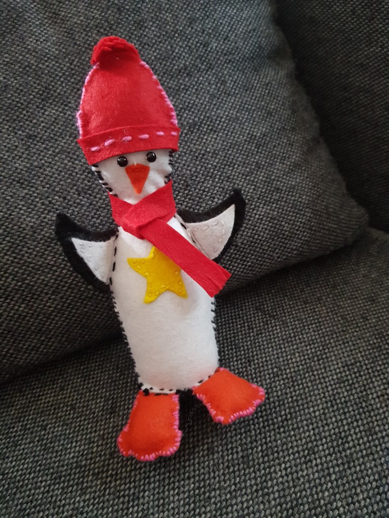 A felt penguin wearing a red hat and scarf.