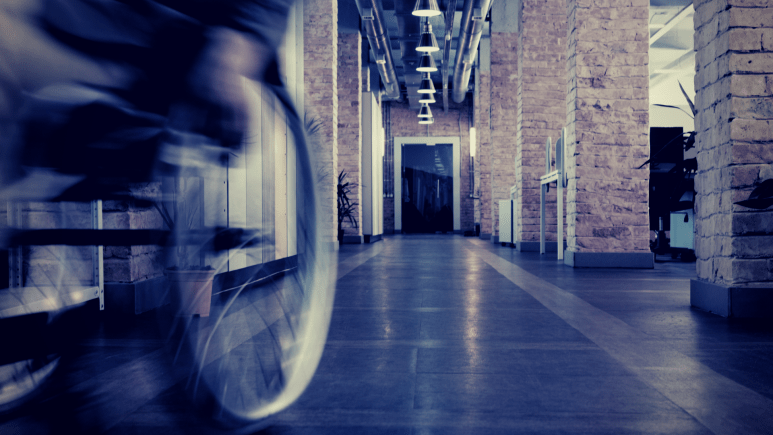 Blurred shot of a manual wheelchair moving towards the left of the camera down a corridor.