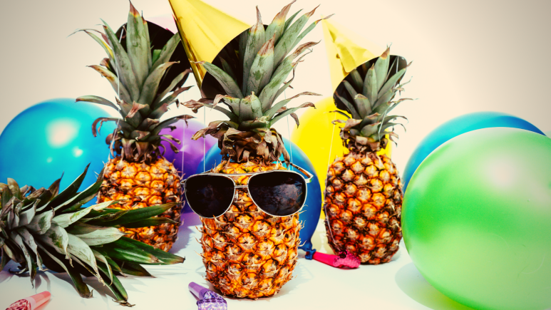 Pineapples sporting party hats and sunglasses among balloons.