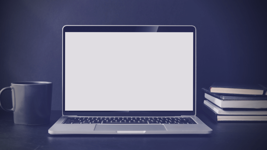 A laptop showing a blank screen, notepads, and coffee mug.