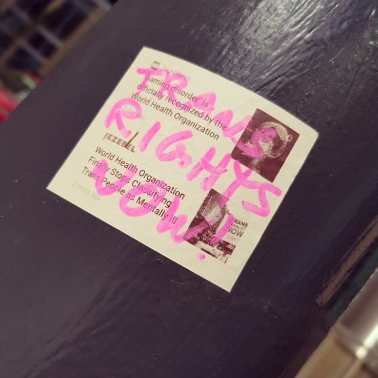 Trans Rights Now scrawled in pink marker, on a sticker on a lamppost in the city centre.