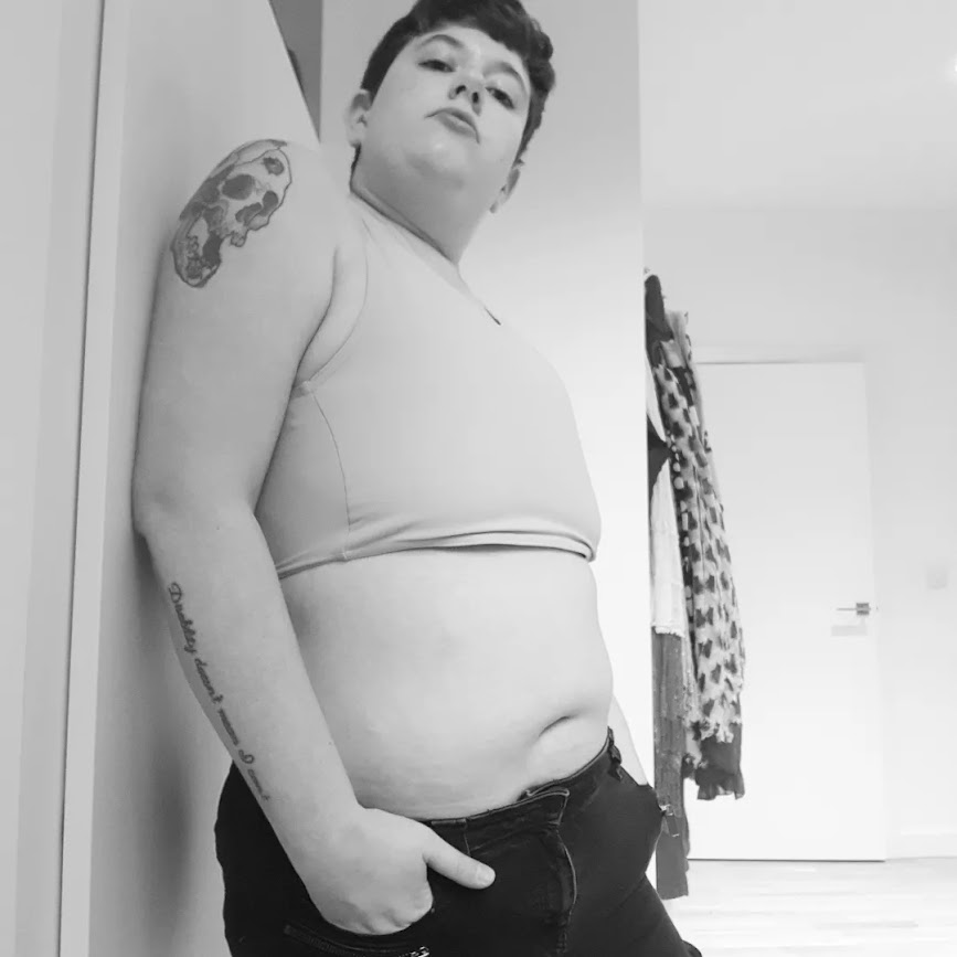 Black and white photograph angled up at me wearing my binder and black jeans.